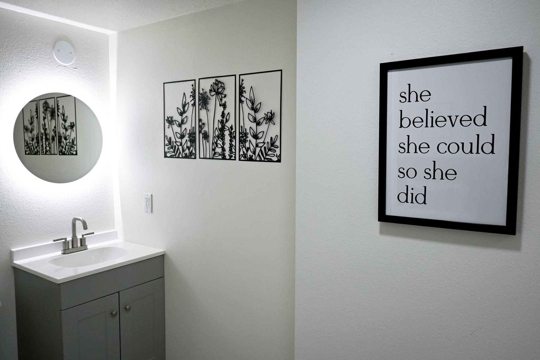 Clean residential bathroom with a backlit mirror and framed art reading she believed she could so she did at the Albuquerque facility
