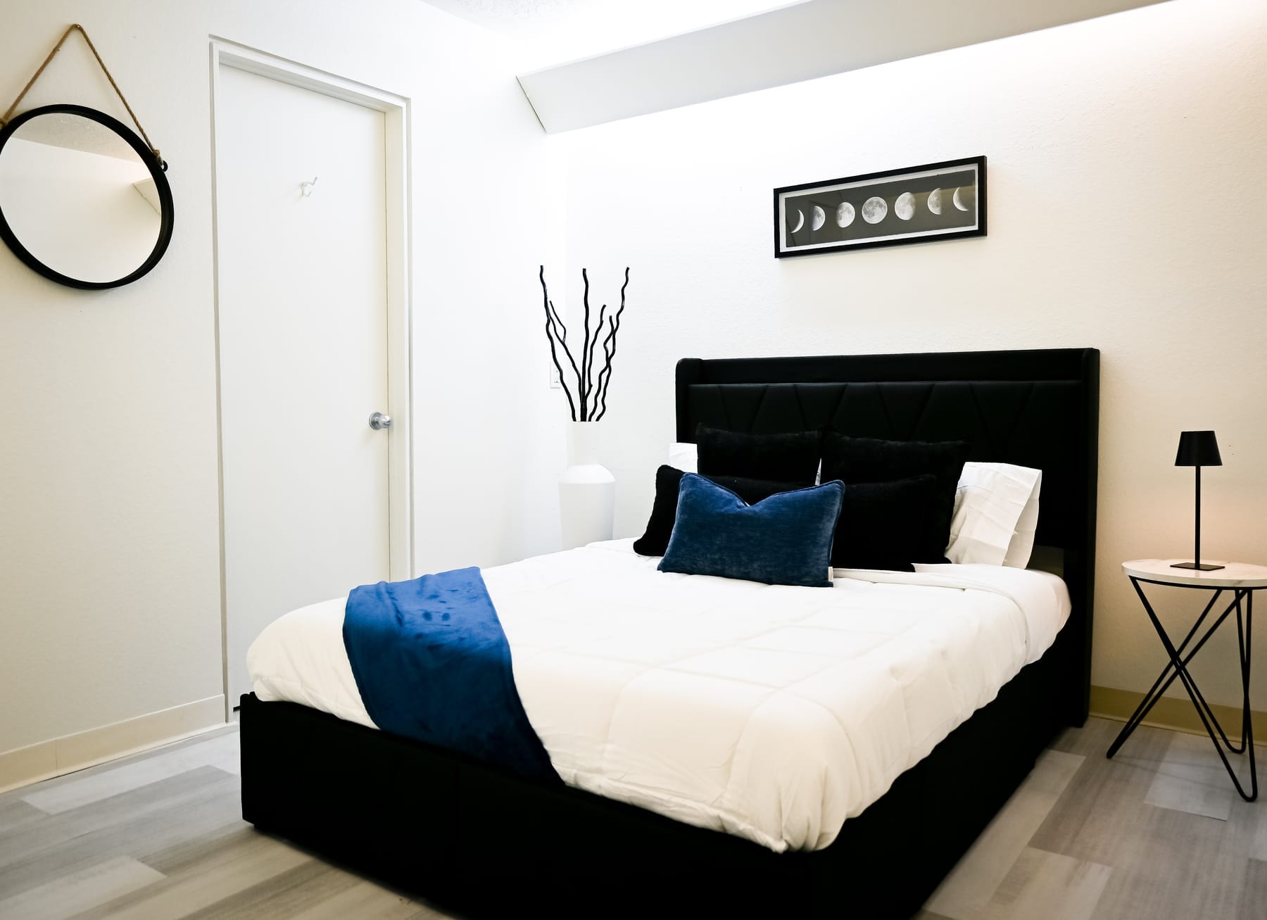 Light-filled residential bedroom with a queen bed, blue throw, and moon-phase artwork at the Albuquerque facility