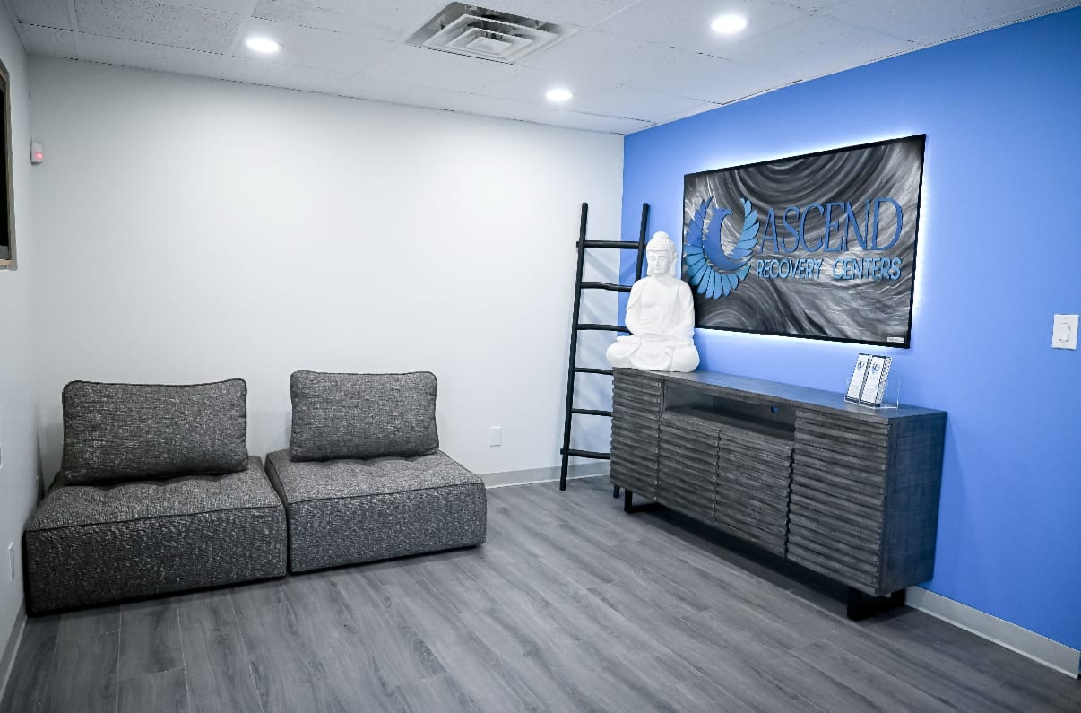 Reception lounge with soft grey seating and the Ascend Recovery Centers sign at the Albuquerque facility
